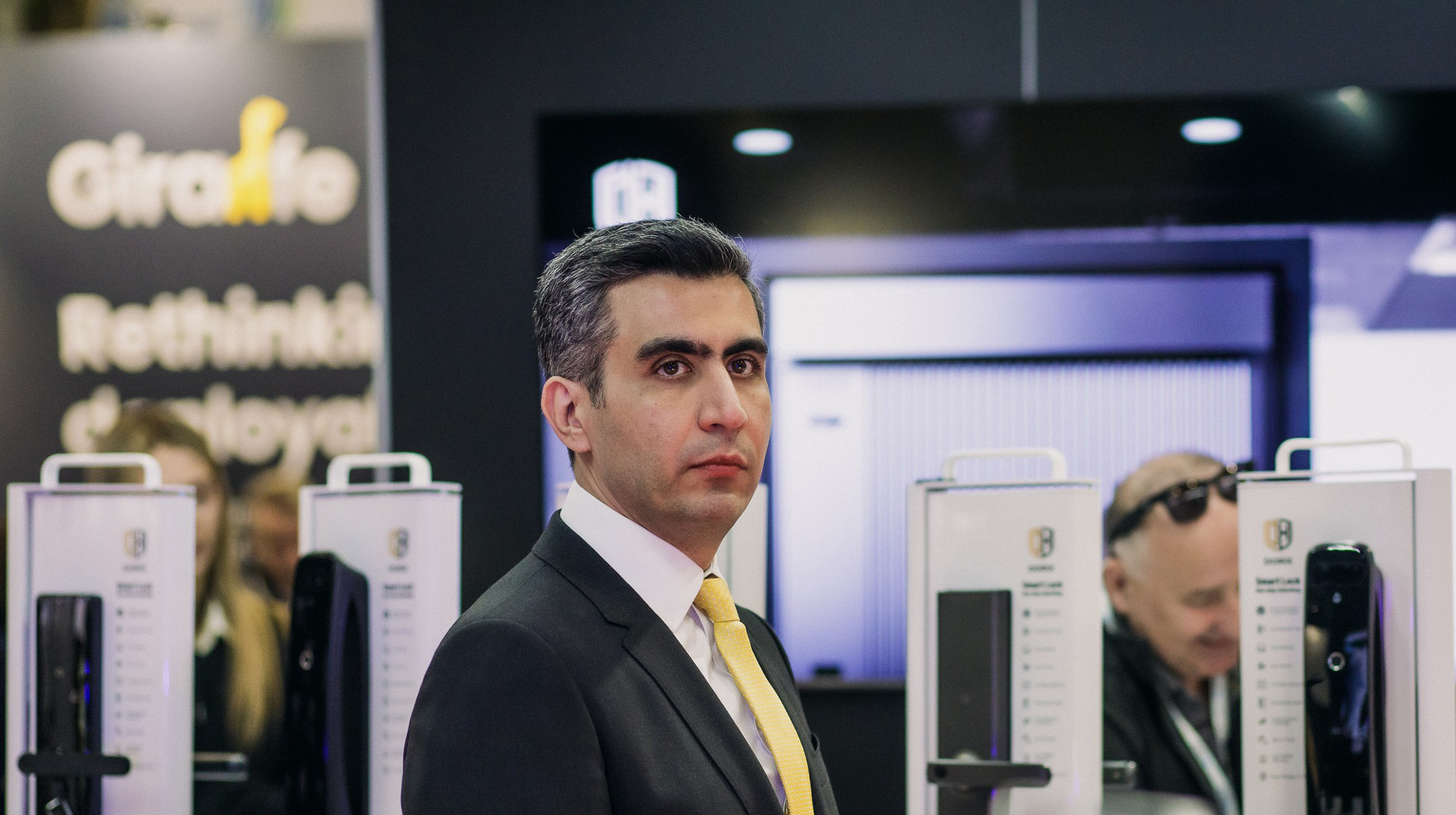 Ali Aydan, Founder and CEO of Dorix, standing at a technology exhibition booth with Dorix products on display, wearing a suit and tie.