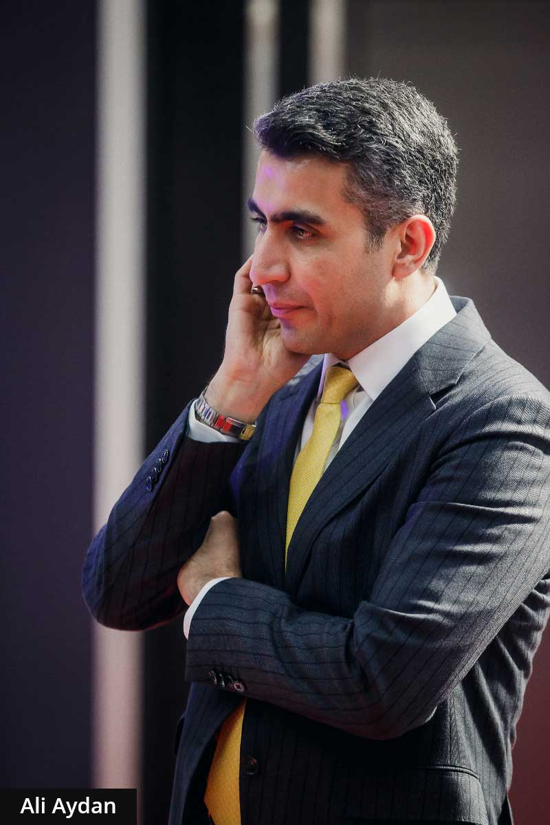 Ali Aydan in a pinstripe suit and yellow tie, captured in a thoughtful, pensive pose during a business event.
