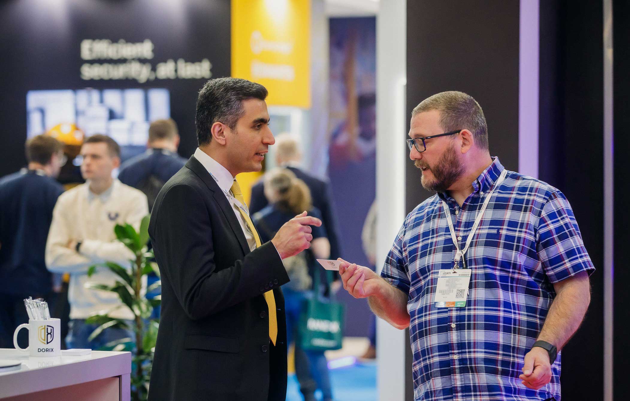Ali Aydan exchanging a business card while discussing security technology solutions at a professional trade fair.